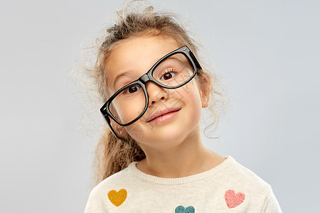 学校,教育视觉微笑的小女孩灰色背景上弯曲放置的眼镜的肖像微笑的小女孩戴着歪戴的眼镜图片