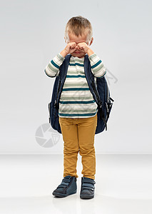学前教育儿童哭泣的小男孩与学校背包灰色背景带着学校背包哭的小男孩图片