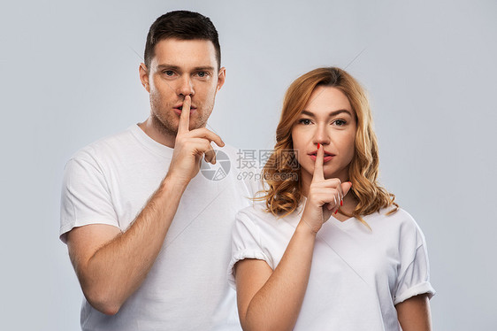 秘密,人的幸福的夫妇白色T恤上着灰色背景上的沉默姿态穿着白色T恤的幸福夫妇着沉默的手势图片