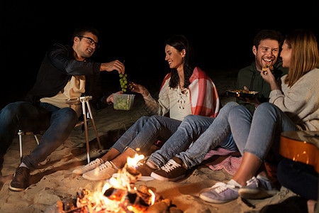 休闲人们的群微笑的朋友晚上海滩上的篝火上野餐朋友们海滩的篝火上野餐图片