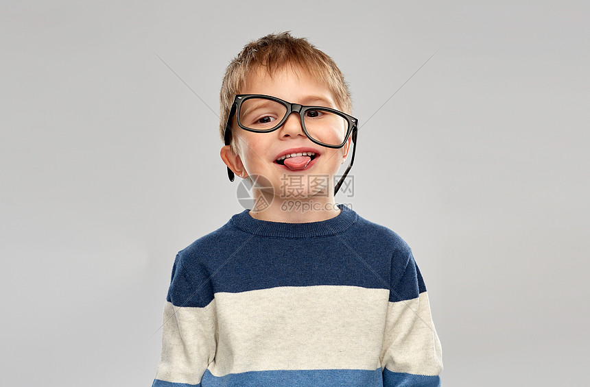 学校,教育视觉微笑的小男孩的肖像,戴着歪歪扭扭的眼镜,灰色的背景上露出舌头戴眼镜的小男孩的肖像,露出舌头图片