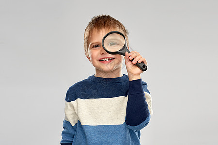调查,发现视觉微笑的小男孩放大镜灰色背景小男孩透过放大镜看图片