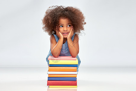 童,学校教育快乐的微笑小非裔美国女孩与堆灰色背景的书籍带着书微笑的非裔美国女孩图片