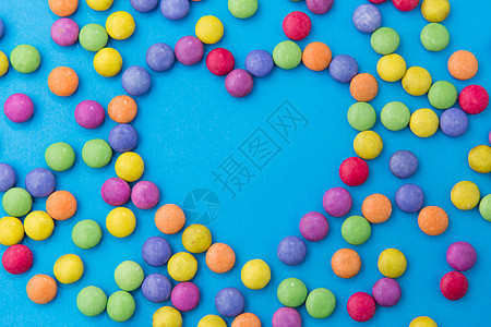 糖果,糖果情人节的明亮的五彩糖果滴形状的心脏蓝色背景糖果滴蓝色背景上的心脏形状背景图片