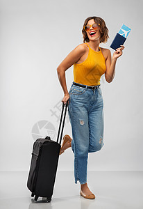 旅行,旅游度假的快乐的笑轻芥末黄色顶部与机票,护照随身携带的灰色背景带着机票旅行袋的快乐轻女人图片