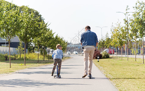 共享自行车家庭,休闲父亲的快乐的父亲花时间小儿子骑滑板车城市快乐的父亲小儿子城市骑滑板车背景