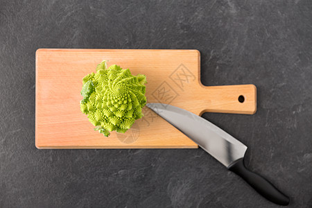 罗曼尼康帝蔬菜,食物烹饪石板石背景上的木制切割板上罗曼斯科西兰花菜刀罗曼斯科西兰花切割板上的刀设计图片
