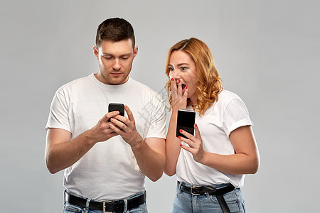 技术人的幸福的夫妇穿着白色T恤与智能手机灰色背景穿着白色T恤智能手机的幸福夫妇背景图片