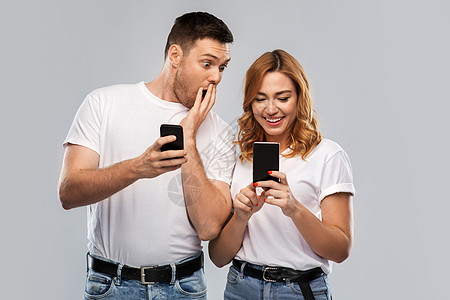 技术人的幸福的夫妇穿着白色T恤与智能手机灰色背景穿着白色T恤智能手机的幸福夫妇图片