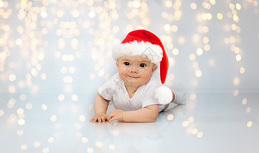 诞节,假日童的可爱的小婴儿诞老人帮助帽子躺地板上的节日灯光背景穿着诞老人帽子的小婴儿躺地板上图片