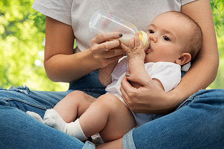 家庭,婴儿人的密切的母亲喂养婴儿与牛奶配方瓶绿色的自然背景用牛奶配方母亲喂养婴儿图片
