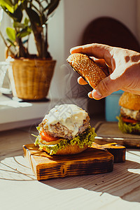 新鲜的自制汉堡蒸汽烹饪,男人把包放奶酪汉堡上,自然光早上厨房里新鲜的自制汉堡图片
