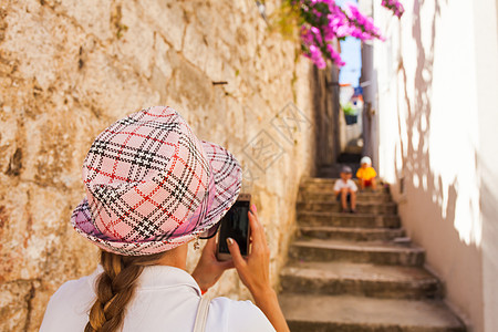 轻的女旅行者戴着顶支票帽子,条古老的狭窄街道上坐楼梯上的照片轻的女旅行者为她的孩子拍照图片