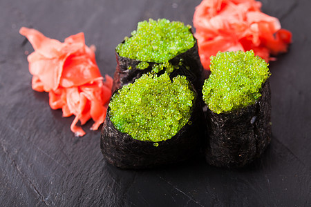 特写托比科绿色黑吉里寿司与飞鱼黑色石板背景托比科绿色寿司红色腌制姜片图片