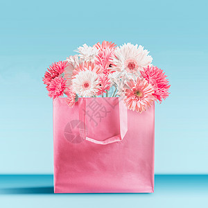 粉彩粉红购物袋与非洲菊雏菊花站桌子上的绿松石蓝墙背景品牌模拟夏季爱,销售推广理念图片