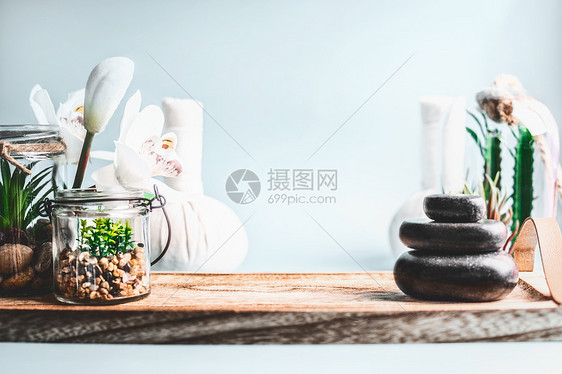 水疗背景堆叠的热石,健康设备与肉质植物白色兰花桌子上的浅蓝色墙壁背景美丽,健康的生活方式身体护理理念图片