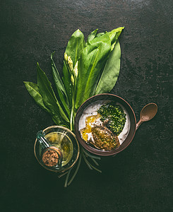 野生大蒜酸奶蘸敷料木制碗黑暗的乡村厨房桌子背景与配料油芥末,顶部视图与健康的季节食品图片