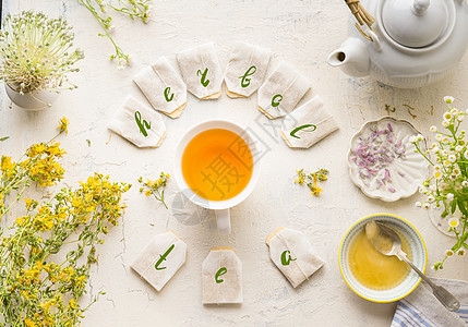 白色杯子与框架茶袋文字草药茶白色桌子背景,顶部视图带茶壶蜂蜜新鲜草药鲜花的草药茶具健康预防饮料治疗图片