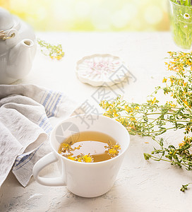 阳光明媚的夏日背景下,白色桌子上的草药茶杯促进免疫消化系统健康的自然疗法图片