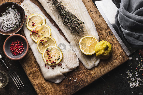生鳕鱼片与柠檬片草药乡村木制切割板,顶部视图鱼烹饪准备健康饮食图片