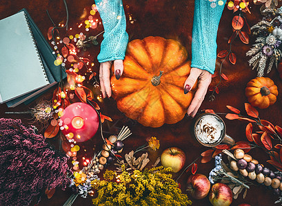 女手穿着针毛衣,黑暗的背景上着大南瓜,秋天安排落叶,燃烧蜡烛,秋天的花朵,苹果,仙女灯,书的风景平躺图片