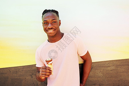 轻英俊的黑人男子穿着件粉红色的t恤,微笑着,夏天着个冰淇淋筒画好的墙上,日出晴天图片