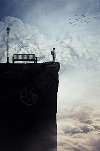 励志想象的风景,个轻的男孩,背上个袋子,站云层上方的悬崖的顶峰上,看着地平线,靠近张长凳盏路灯人生旅程机图片