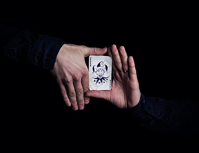 双手紧握小丑扑克牌魔术师黑色背景上用卡片展示他的把戏图片