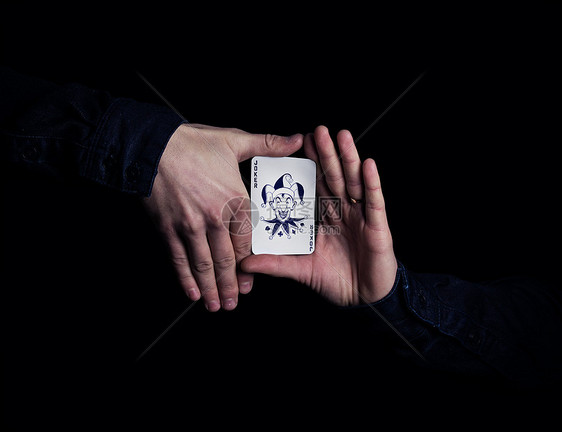 双手紧握小丑扑克牌魔术师黑色背景上用卡片展示他的把戏图片