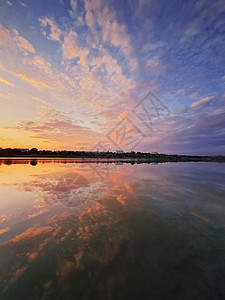垂直拍摄蓬松的彩色云,反射湖上的日落平静,田园诗般的黄昏场景,池塘上很多云图片