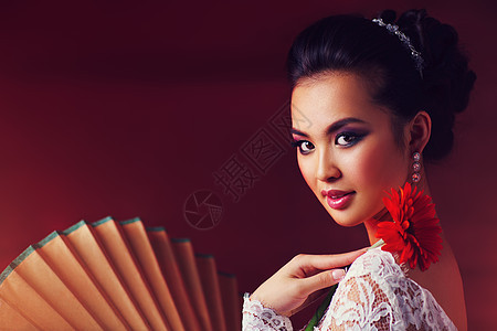 轻的亚洲女人,红色背景上花扇子肖像轻的亚洲女人图片