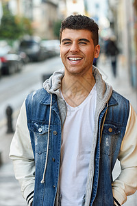 轻的男人,蓝色的眼睛白色的牙齿街上时尚模特城市背景下微笑,穿着白色T恤,牛仔裤蓝色夹克图片