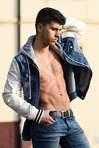 英俊的轻人,肌肉发达的身体街上城市背景的时尚模特穿着牛仔裤蓝色夹克背景图片