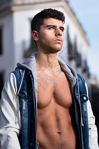 英俊的轻人,肌肉发达的身体街上城市背景的时尚模特穿着牛仔裤蓝色夹克图片