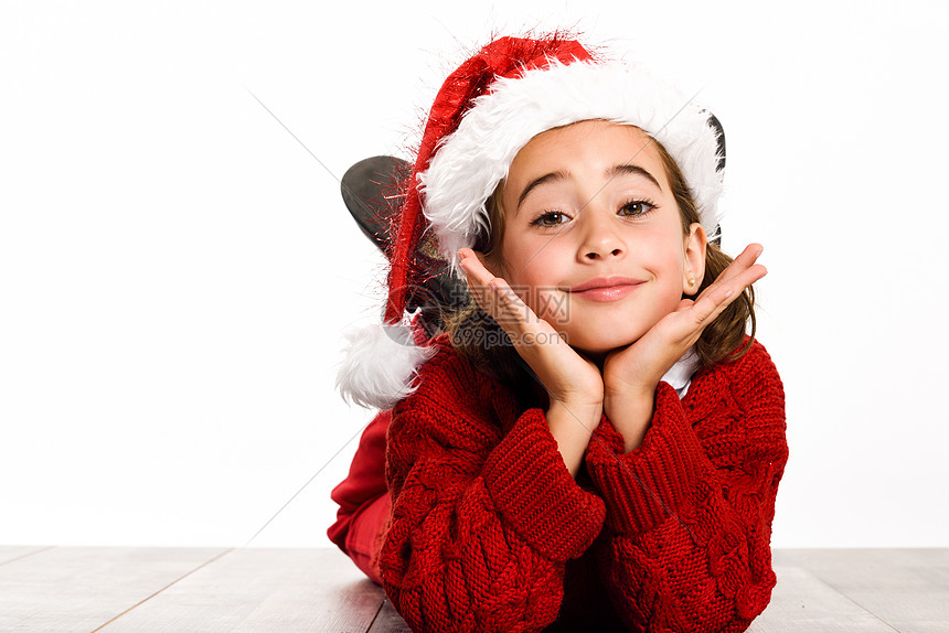 可爱的小女孩戴着诞老人的帽子,躺白色背景的木地板上冬天的衣服图片