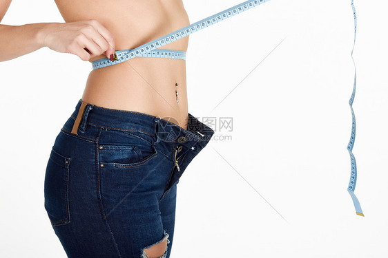 轻的女人用胶带测量腰部穿着白色背景的蓝色牛仔裤的健康女孩图片