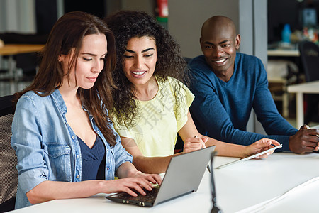 三个轻人白色桌子上用笔记本电脑学漂亮的女孩男人穿着休闲服工作多族裔群体图片