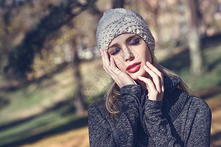 轻的金发女人站个秋天颜色的公园里穿着冬天灰色连衣裙羊毛帽子的漂亮女孩女,直发,眼睛闭上深色眼影图片