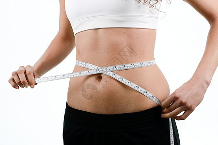 轻的女人节食考虑减肥,用白色背景上的胶带测量腰部图片