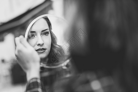 轻女人城市背景中的小镜子里看自己的肖像黑白照片背景图片