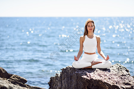 坐在海边石头上练瑜伽的外国女生背景图片