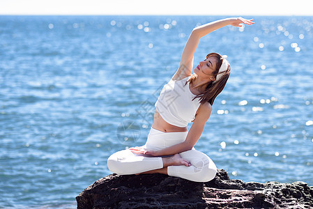 轻的女人海滩上瑜伽女穿着白色运动服,穿着莲花身材,的海洋背景图片