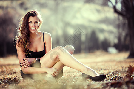 位漂亮女人坐草地上的城市公园里微笑的肖像图片