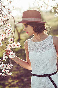 春天花田里轻女人的肖像杏仁花开花了穿着白色连衣裙太阳帽的女孩图片