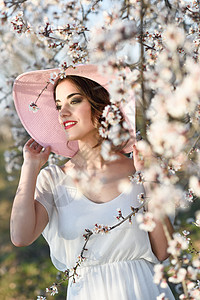 春天花田里轻女人的肖像杏仁花开花了穿着白色连衣裙粉红色太阳帽的女孩图片