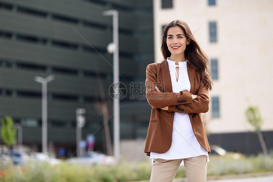 轻的女人,留着漂亮的头发站办公楼外穿正式服装的女商人,留着波浪式发型穿着棕色夹克裤子的轻女孩图片