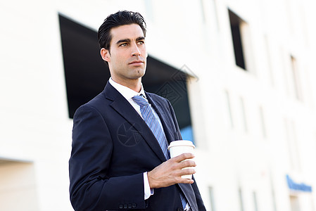 商人正式的衣服,喝咖啡,带着外卖杯穿着蓝色西装城市背景领带的男人图片