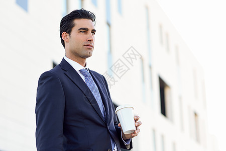 商人正式的衣服,喝咖啡,带着外卖杯穿着蓝色西装城市背景领带的男人图片