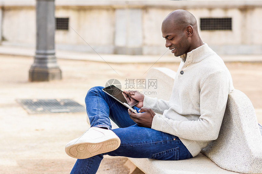 黑人轻人城市背景下看平板电脑智能手机轻的非洲人光头穿着休闲服图片