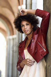 轻的黑人女,留着AFRO发型,站城市街道上混合女人穿红色皮夹克白色连衣裙与城市背景背景图片